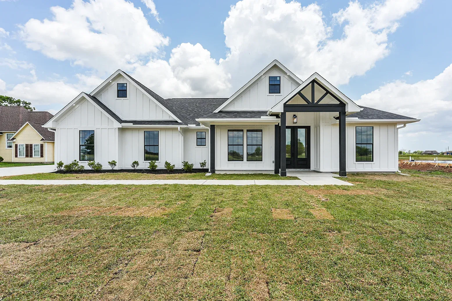 A large white house with a black roof is sitting on top of a lush green field.