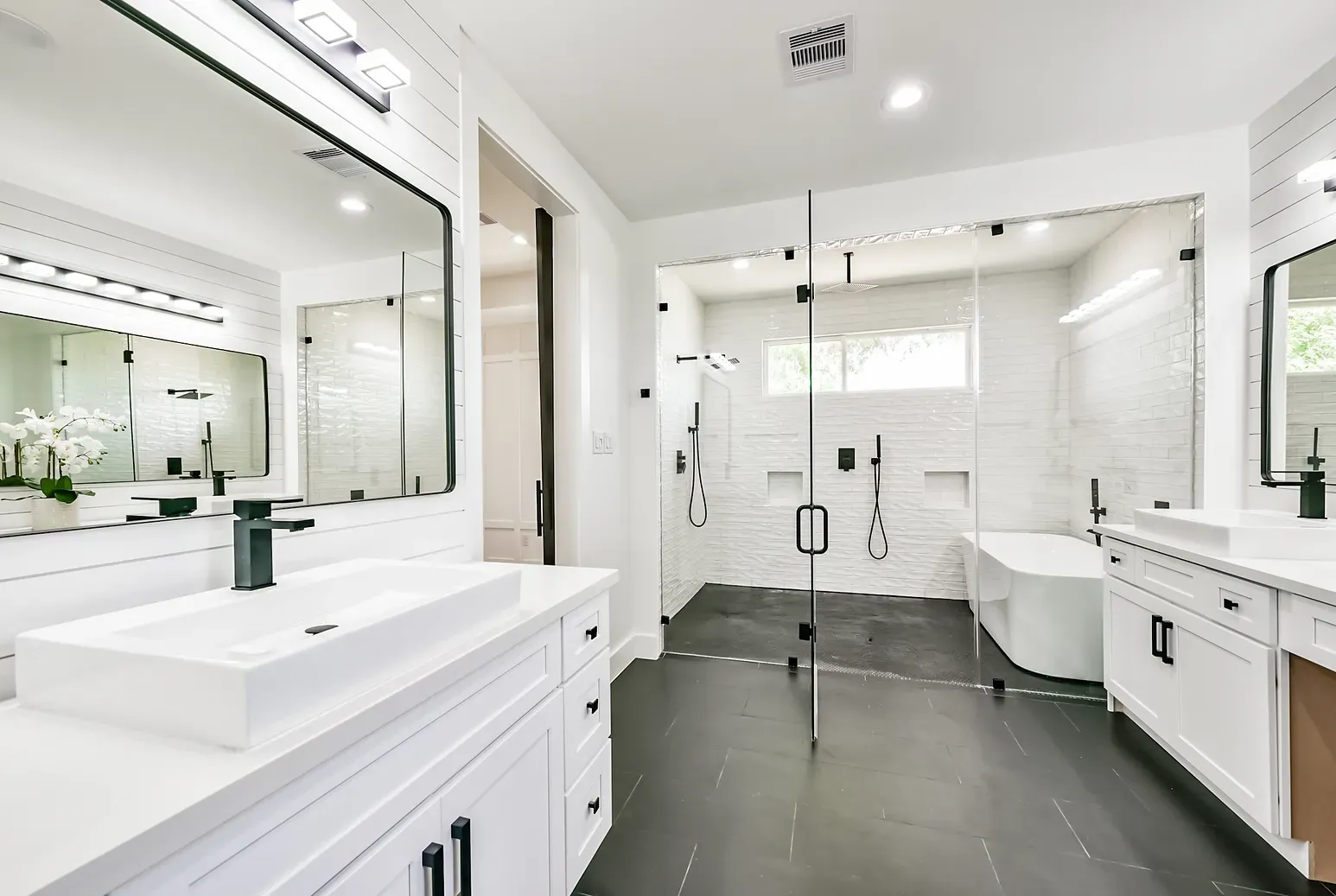 A bathroom with two sinks , two mirrors , a tub and a walk in shower.