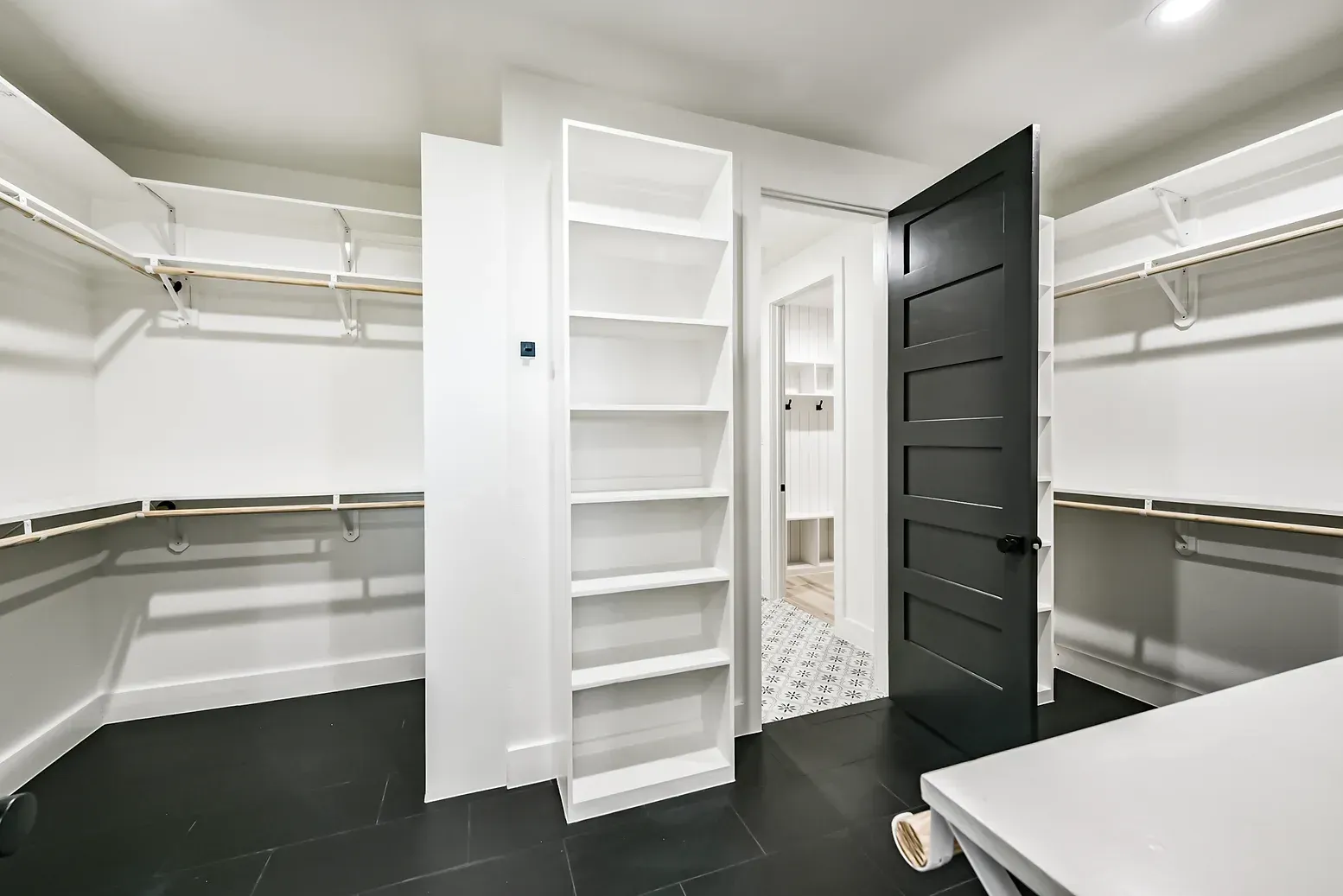 A walk in closet with white shelves and a black door.