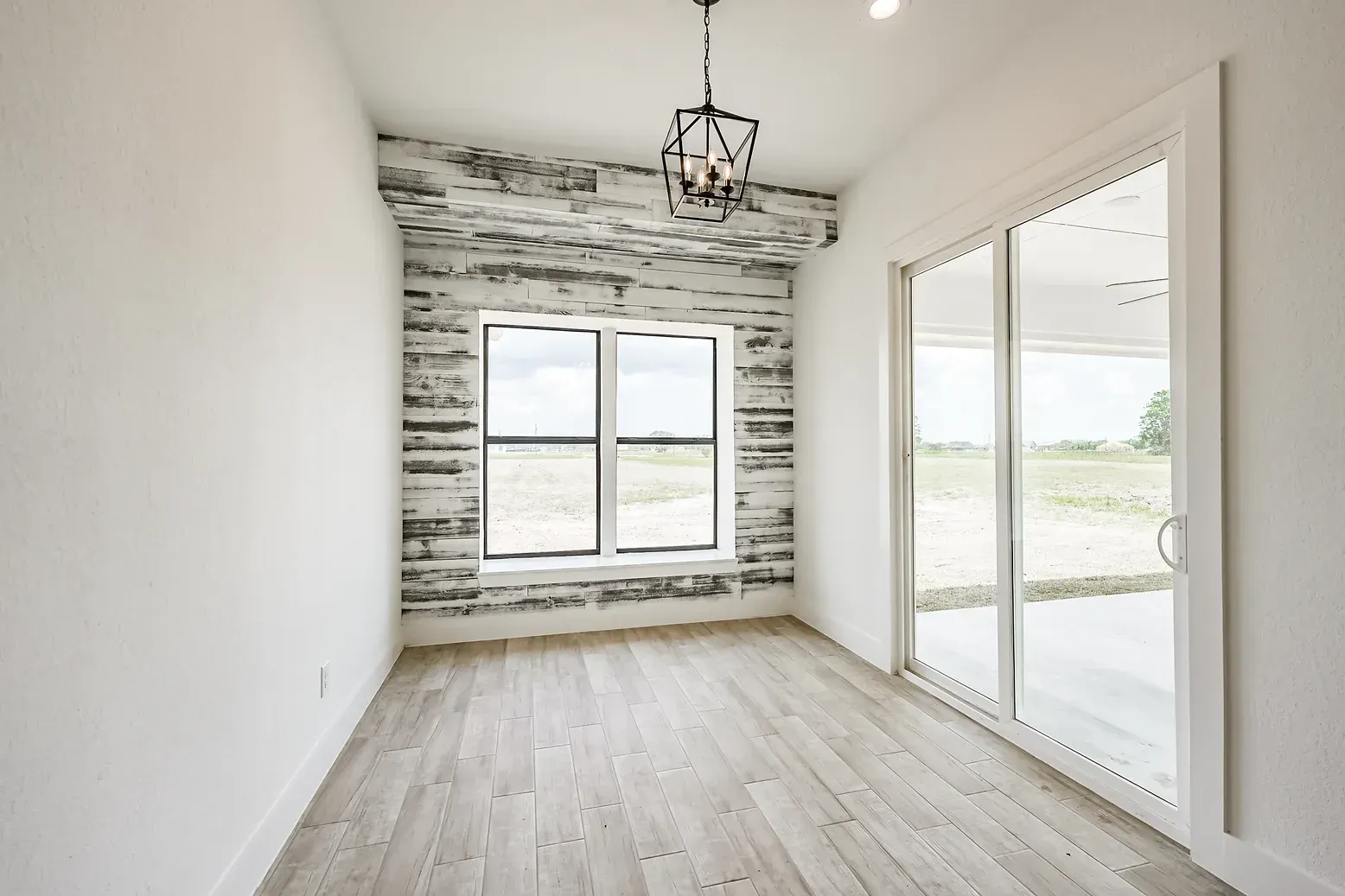 An empty room with sliding glass doors and a chandelier hanging from the ceiling.