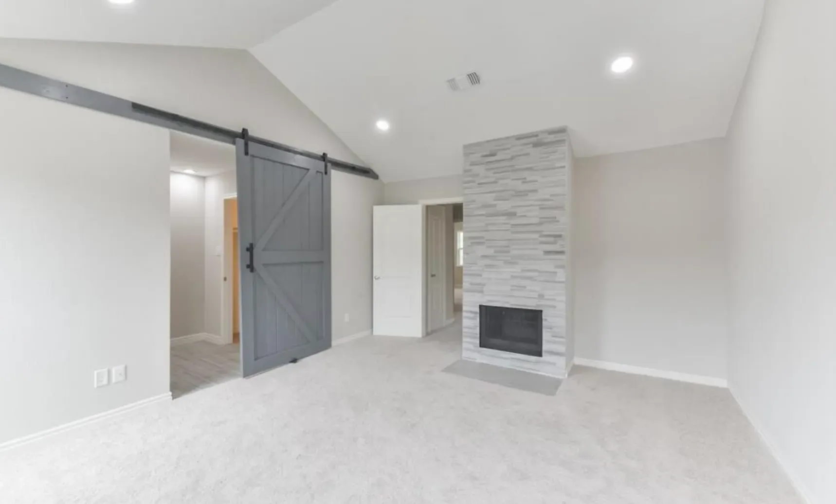 An empty living room with a sliding barn door and a fireplace.