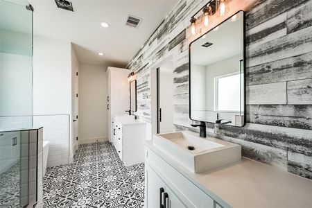 A bathroom with two sinks , a mirror and a walk in shower.