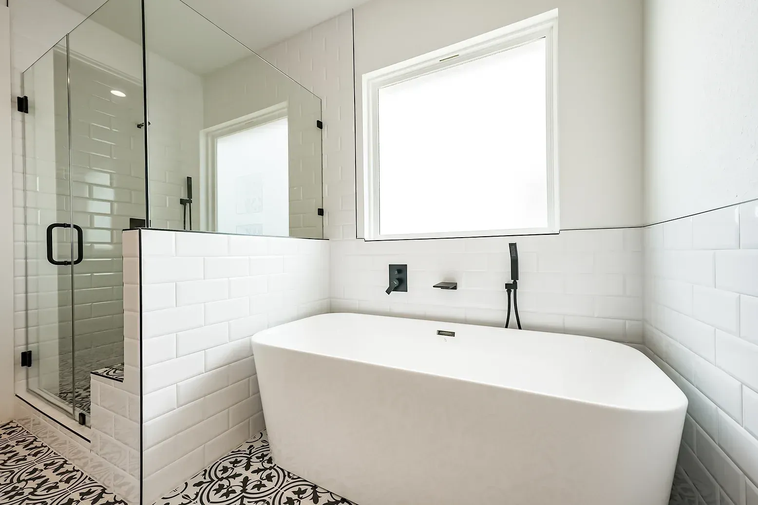 A bathroom with a tub , shower , mirror and window.