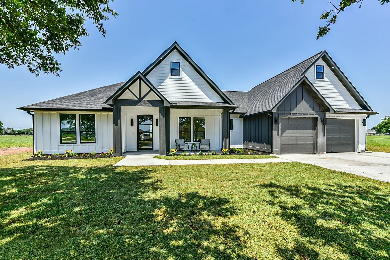 A large white house with a gray roof is sitting on top of a lush green field.
