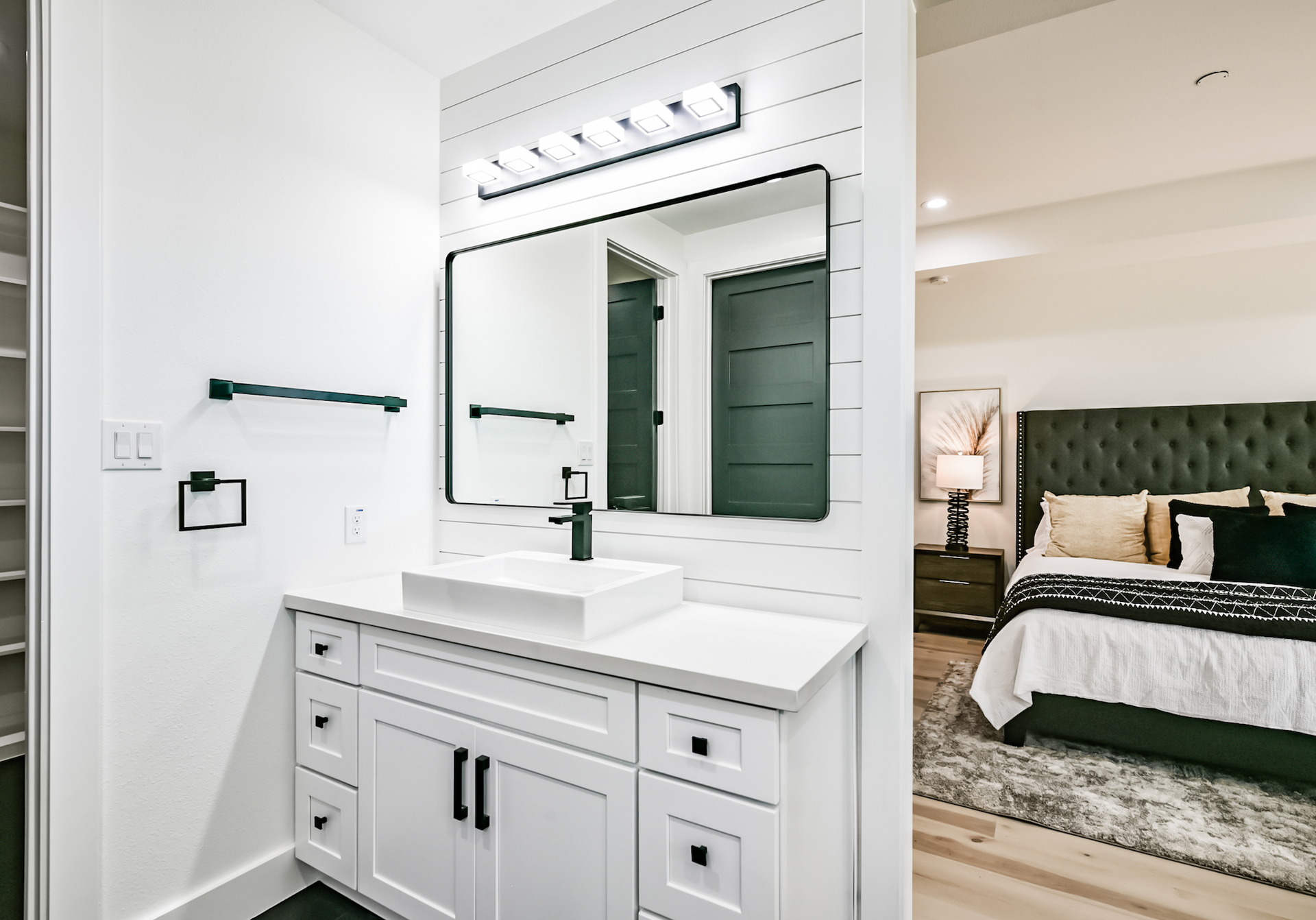 A bathroom with a sink and a mirror next to a bedroom.
