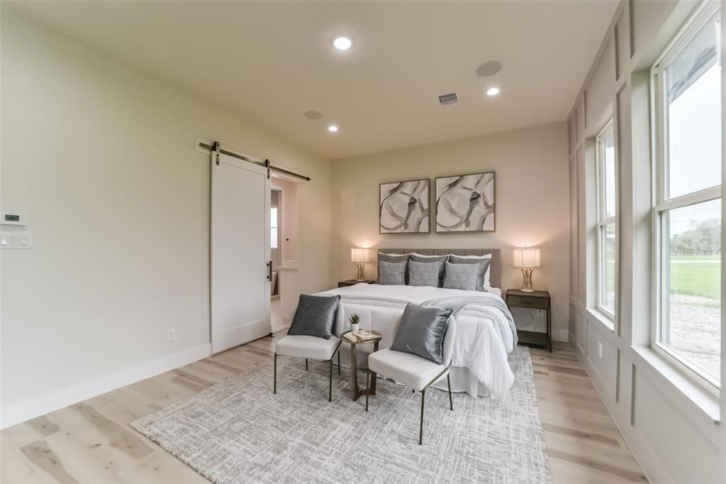 A bedroom with a large bed , chairs , and a sliding barn door.