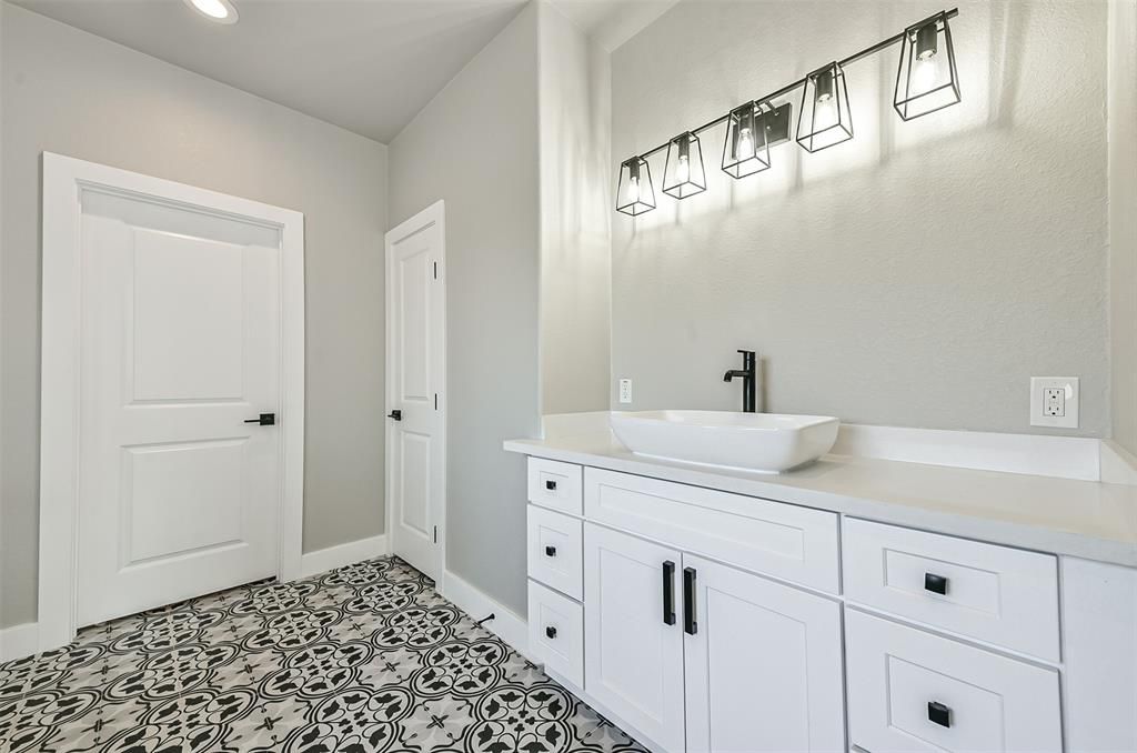 A bathroom with white cabinets , a sink and a mirror.