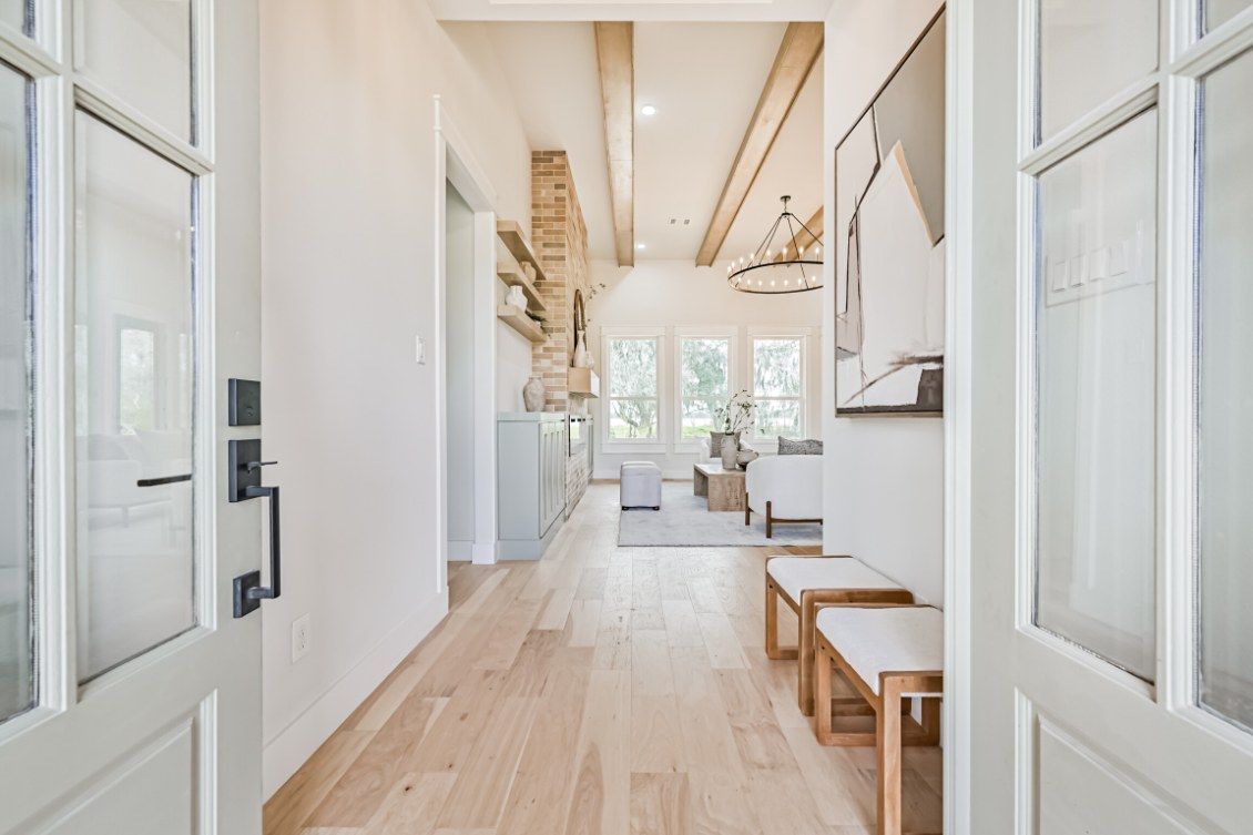 Entryway view through open glass-paneled doors looking into a bright living room with light wood floors and wood beams.