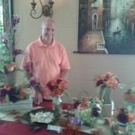 Man standing behind a table of colorful flower arrangements in a decorated room