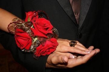 Hands holding with red roses and a decorative bracelet on a dark suit background