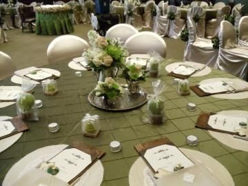 Round banquet table with white chairs, floral centerpiece, and place settings in a decorated event hall