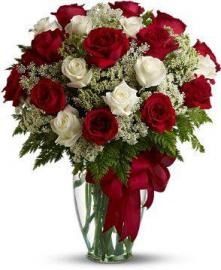 Red and white roses arranged in a tall glass vase with a red ribbon bow