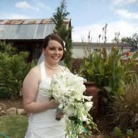Bride in white dress holding a white bouquet outdoors near a rustic building