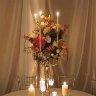 Candles and a floral centerpiece on a round table, with draped curtains in the background
