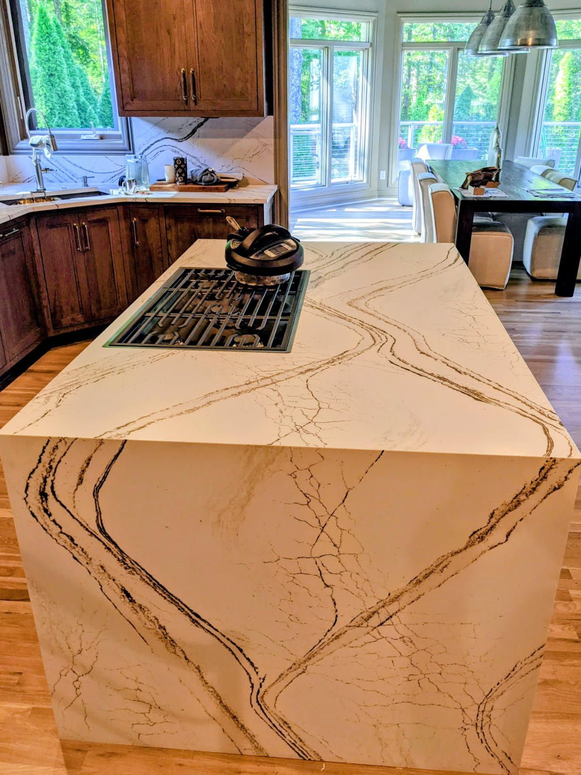 A bright, modern kitchen with white cabinets, a stone island with dark wooden stools, and light wood flooring.
