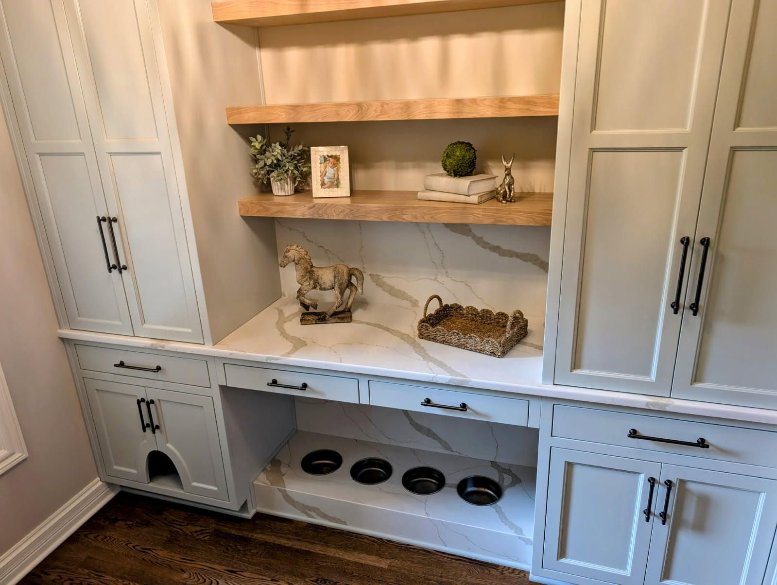 A person in a white t-shirt uses a power drill to install tiles on a wall in a room under construction.