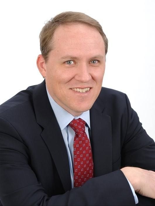 A smiling doctor in a lab coat with a stethoscope around his neck.