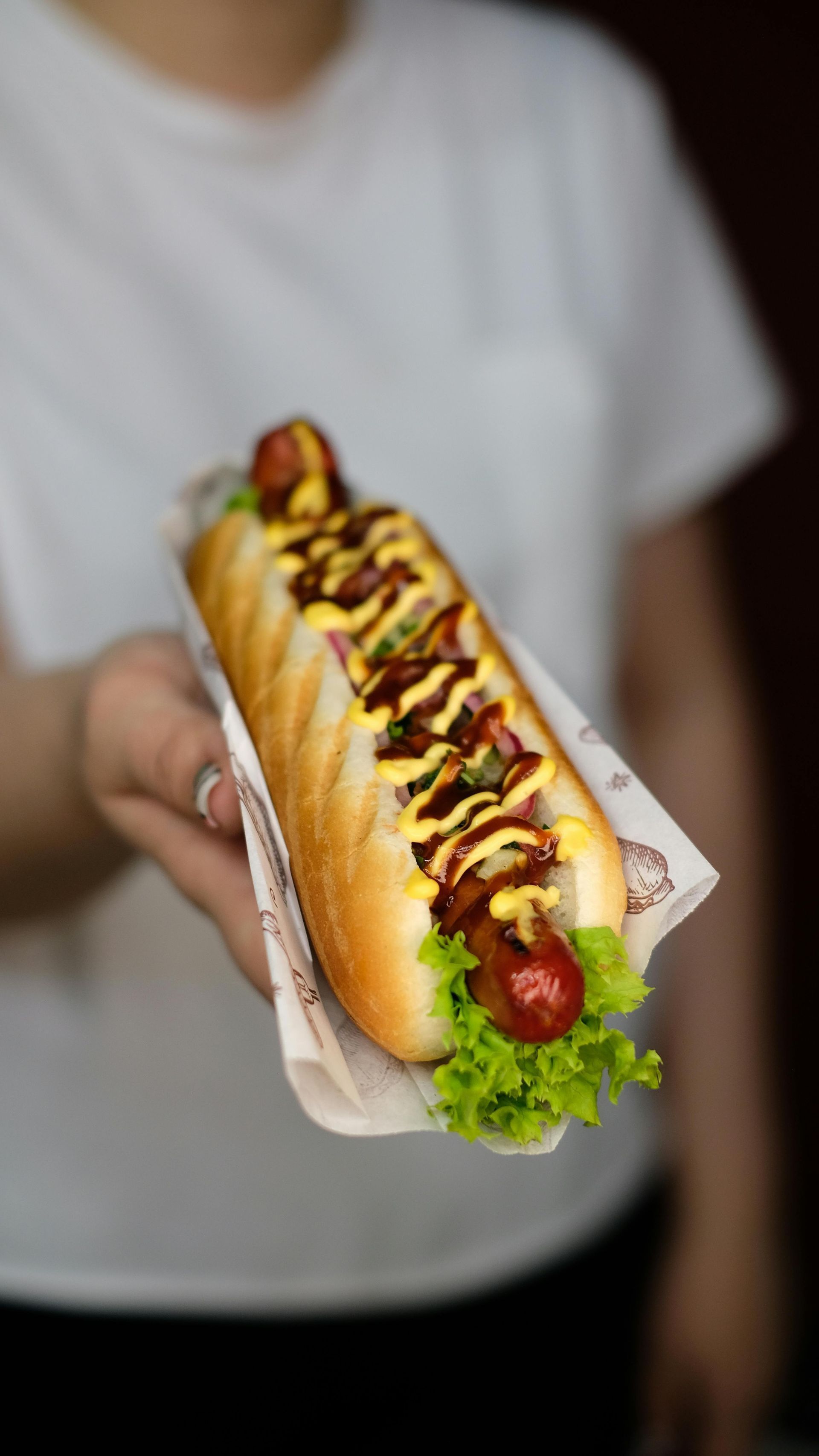 Eine Person hält einen Hotdog mit Salat, Senf und Ketchup.