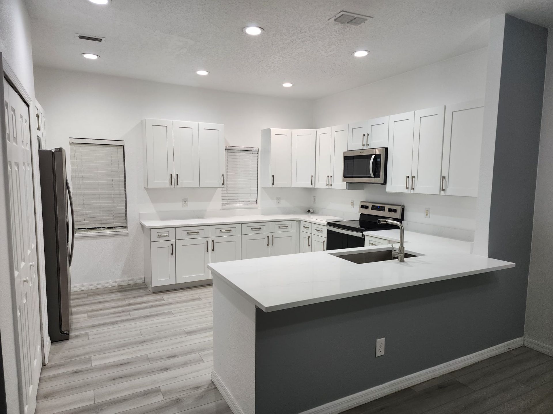 Modern kitchen with white cabinets, light countertops, stainless steel appliances, and dark gray accent walls.