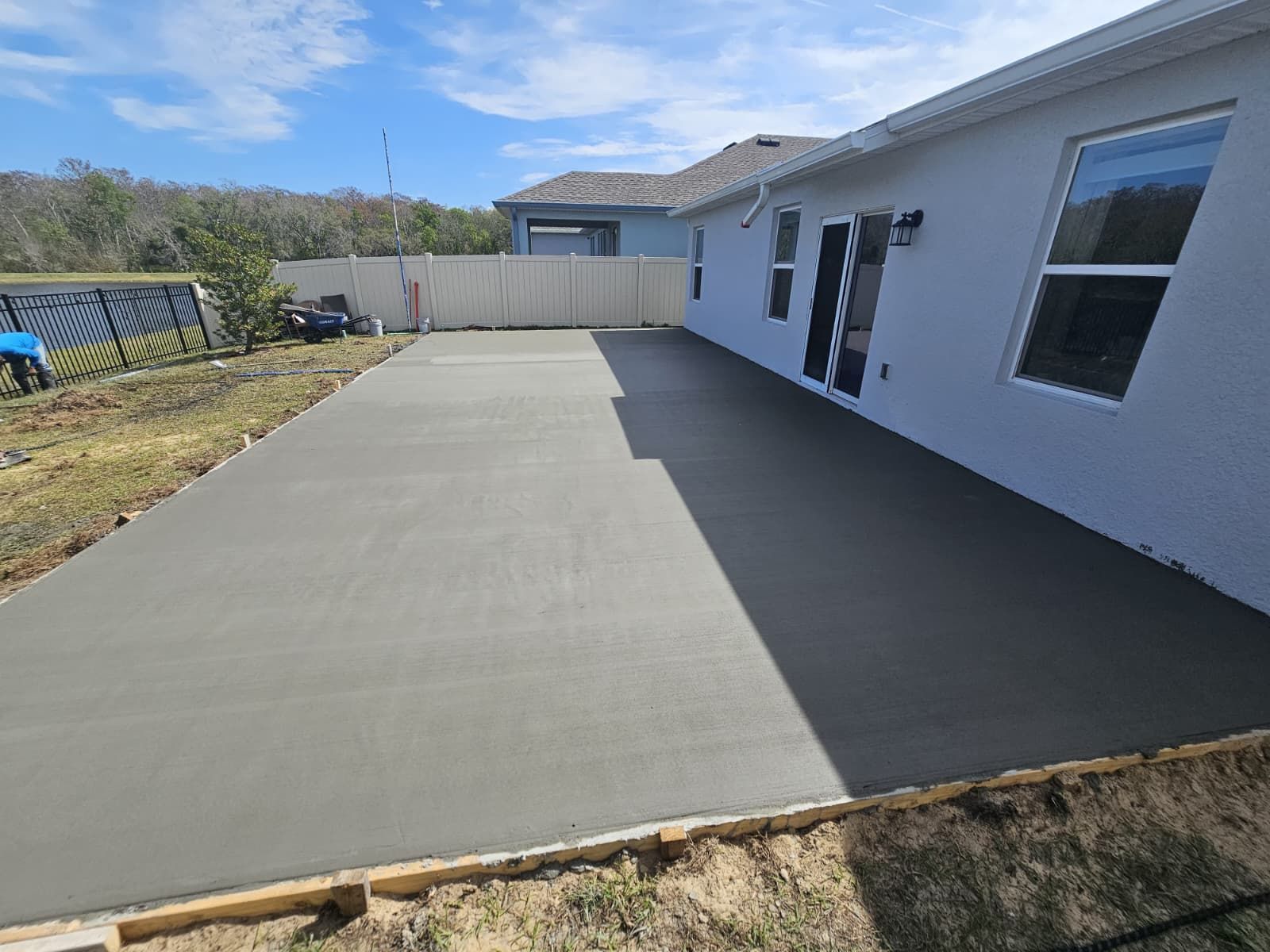 A newly poured concrete patio adjacent to a light-colored house with wooden forms still in place.