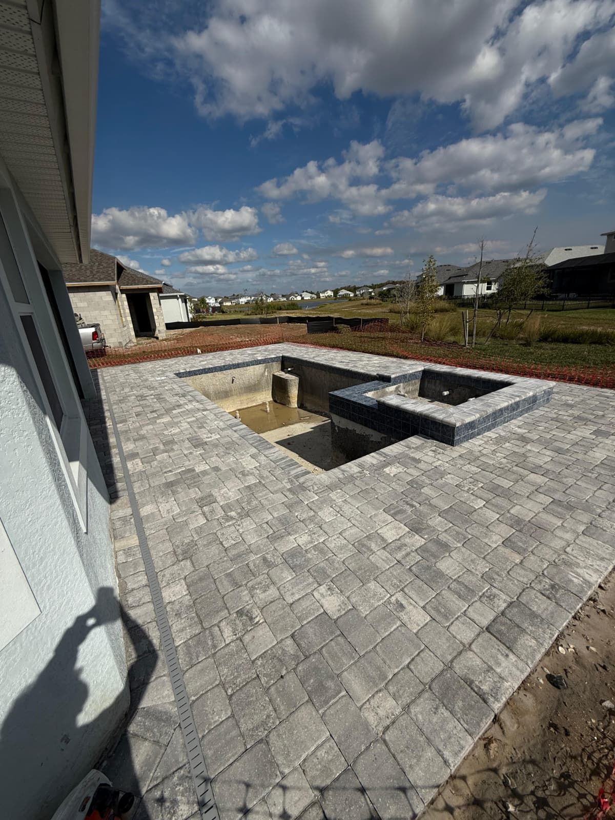 A backyard patio with gray pavers surrounds an unfinished, rectangular swimming pool and a raised, dark-tiled spa.