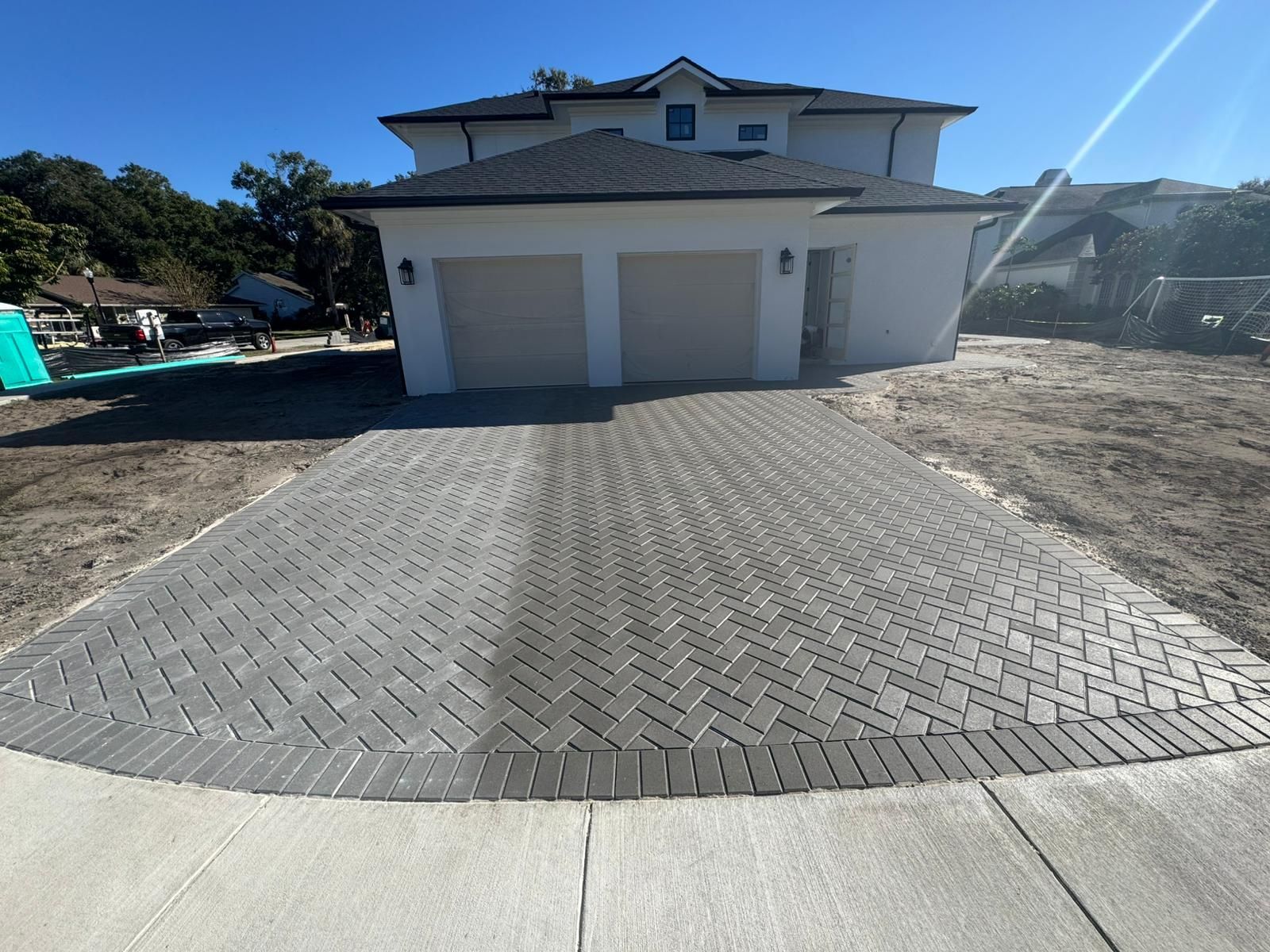 A newly installed gray herringbone-pattern brick driveway leads to a two-car garage of a modern white suburban house.