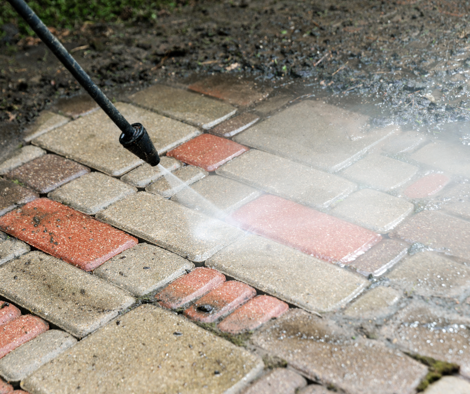 Person pressure washing a brick patio in a sunny yard.