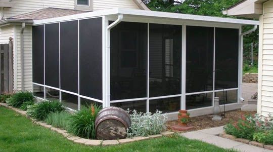 Screened-in porch attached to a house. Black screens, white trim, with landscaping and an old barrel in front.