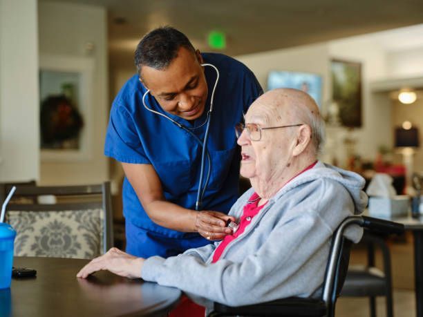 A nurse is examining an elderly man in a wheelchair with a stethoscope