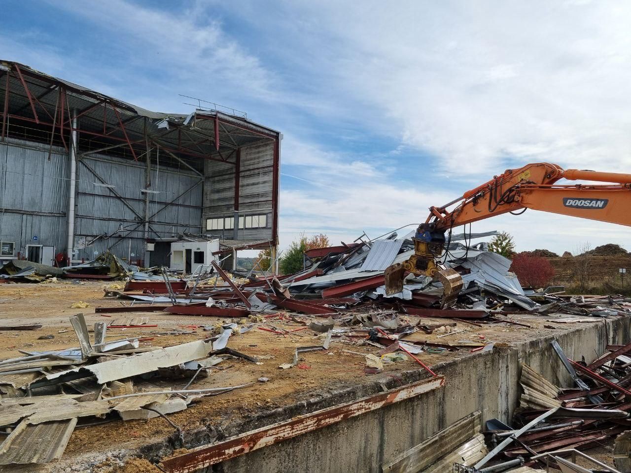 Une grande pelle orange est en train de démolir un grand bâtiment.