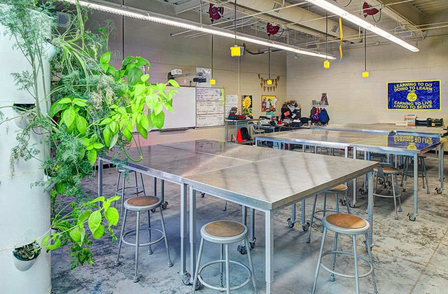 a classroom with tables and stools and a plant hanging from the ceiling .