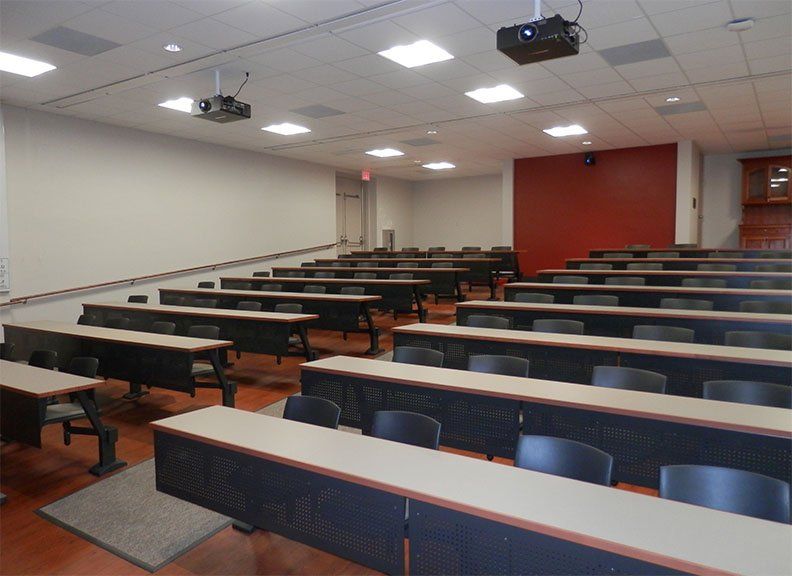 an empty lecture hall with long tables and chairs and a projector