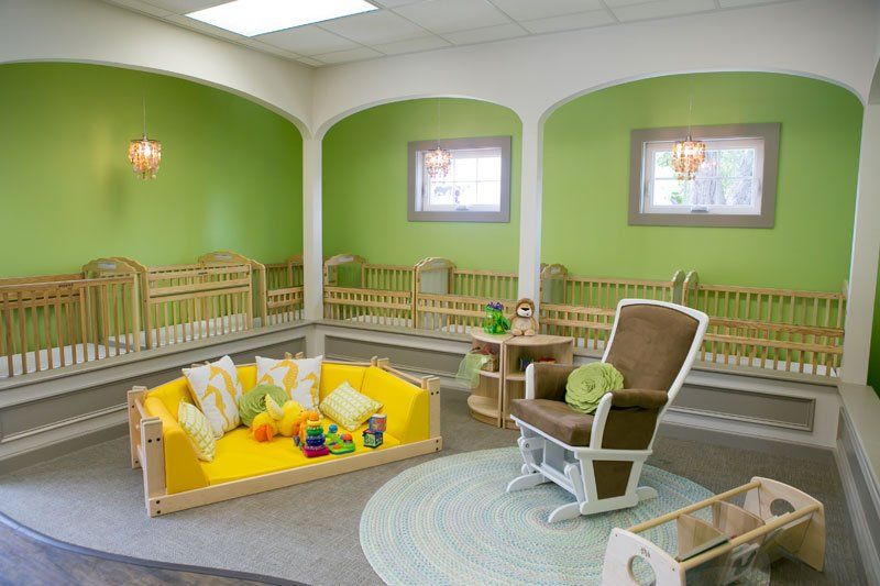 a room with green walls , a yellow couch , a rocking chair , and cribs .