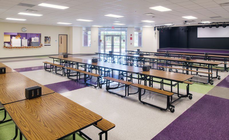 a school cafeteria with tables and benches and a stage .