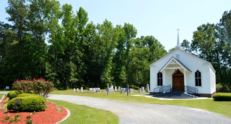 a small white church is surrounded by trees and a graveyard .