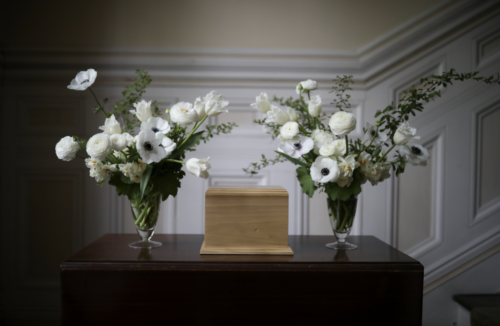 two vases filled with white flowers are sitting on a table next to a wooden urn .