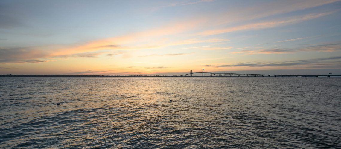 A sunset over a body of water with a bridge in the distance.