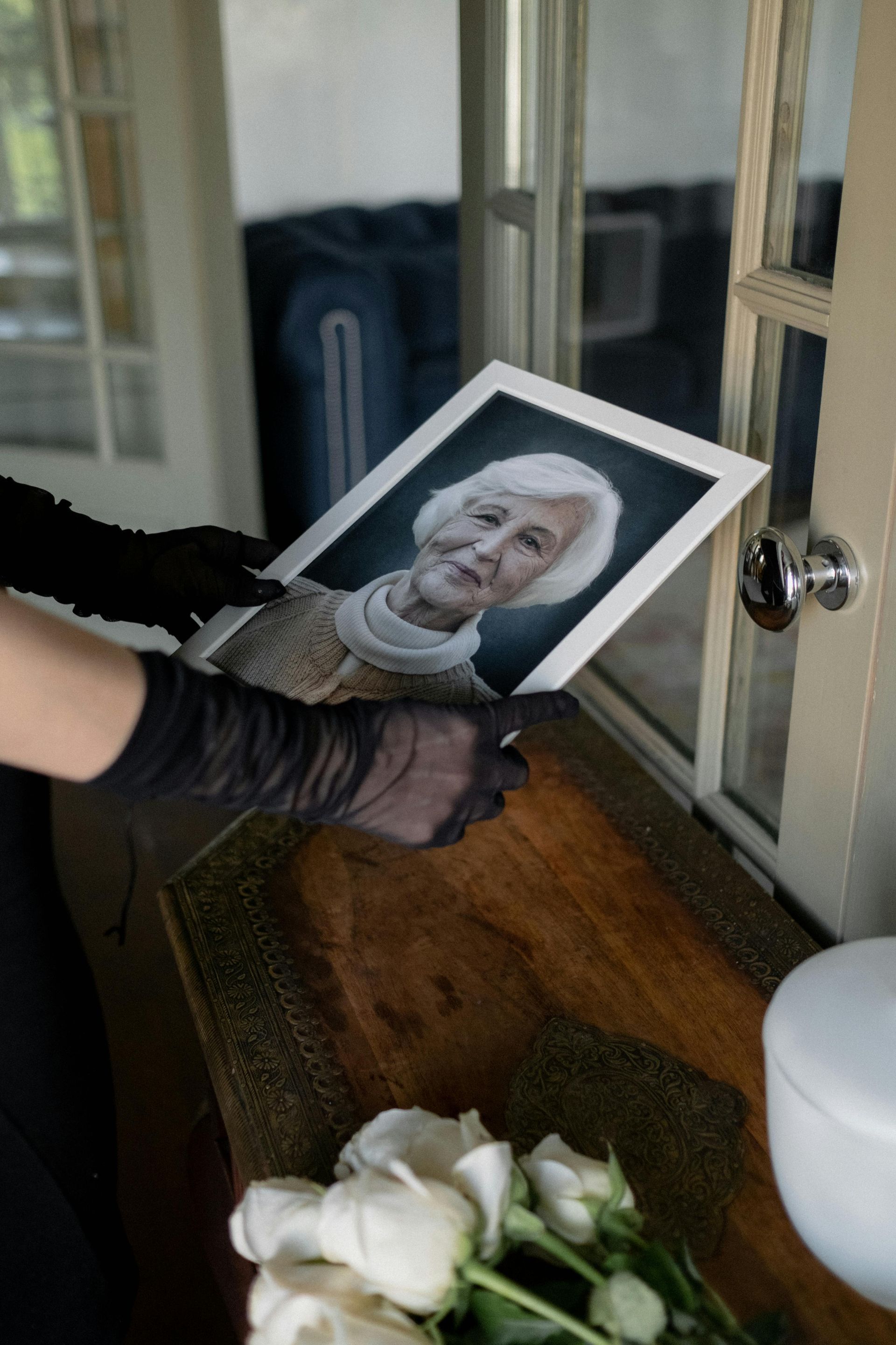 A woman in black gloves is holding a picture of an older woman.