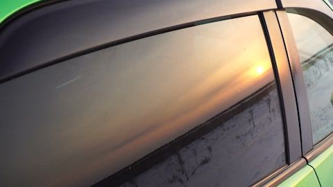 Close-up of a car window reflecting a sunset sky and roadside silhouette