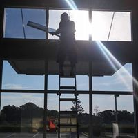 Silhouetted worker on a ladder cleaning windows in a sunlit glass building interior
