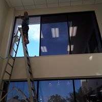 Person on a ladder cleaning tall office windows inside a building