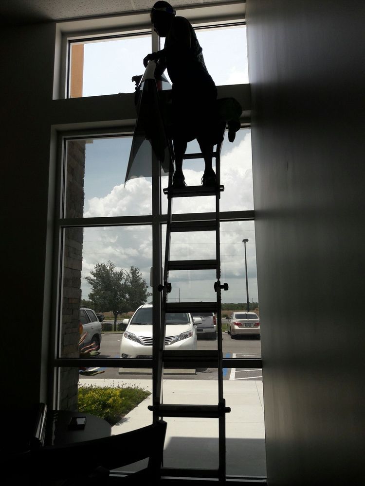 Person on a ladder cleaning a high window in a bright indoor entryway