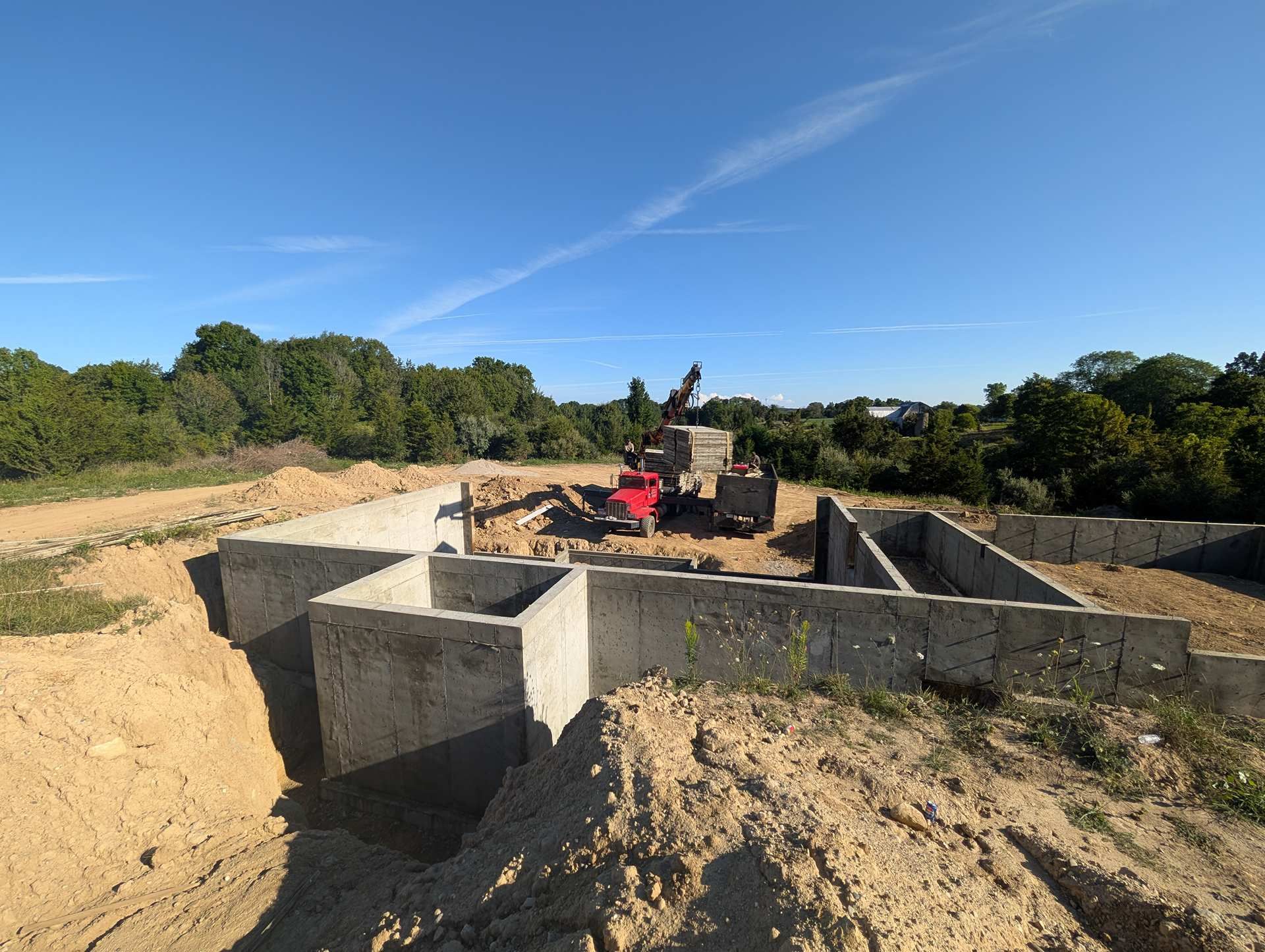 Concrete foundation walls for a building under construction, surrounded by excavated dirt under a clear blue sky.