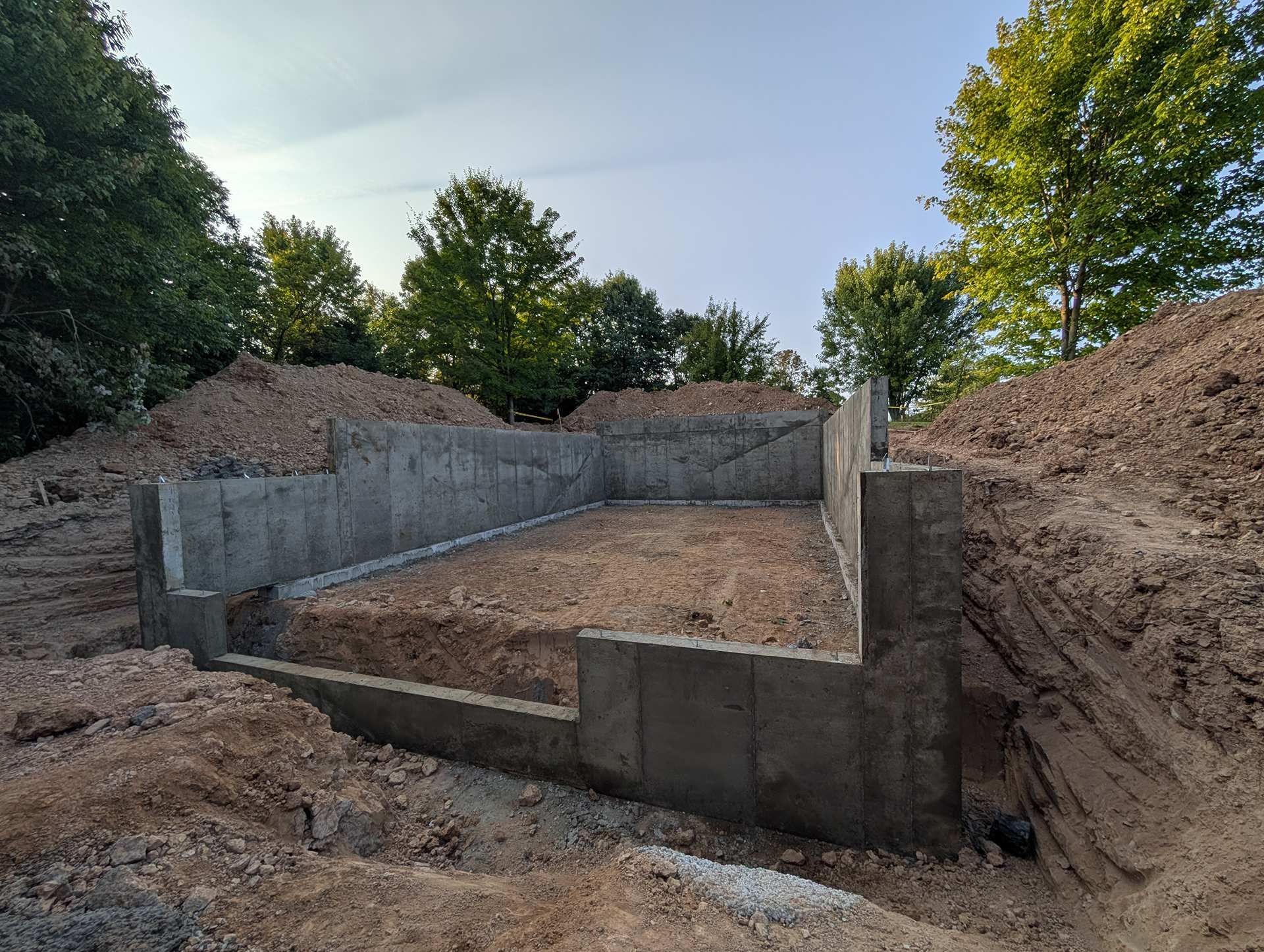 Concrete foundation walls for a new building under construction, surrounded by piles of dirt under a clear blue sky.