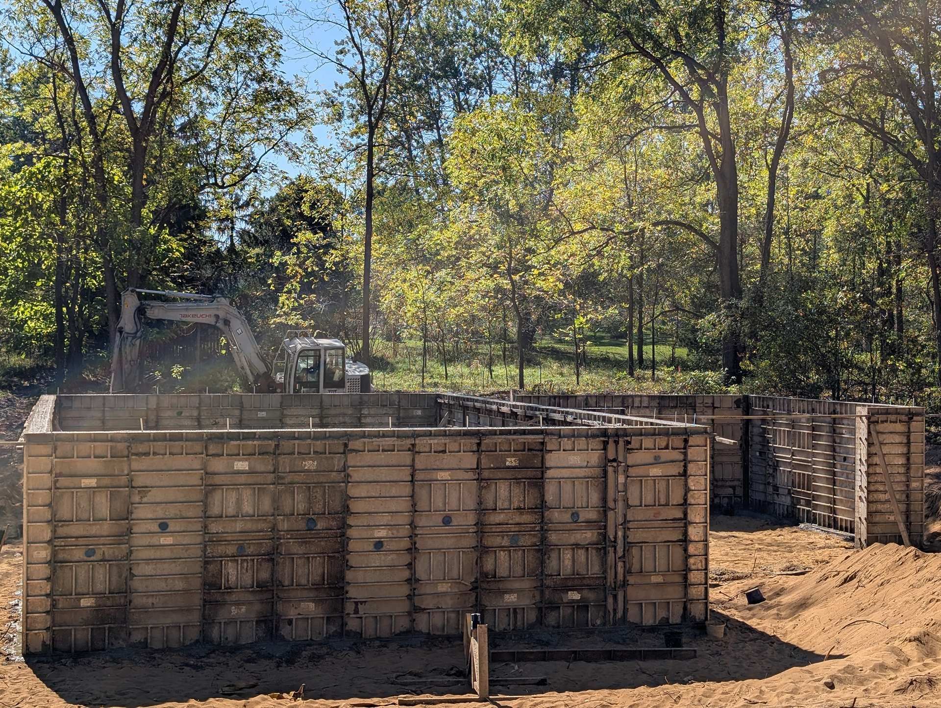 Construction site featuring wooden concrete forms for a building foundation with an excavator parked in the background.