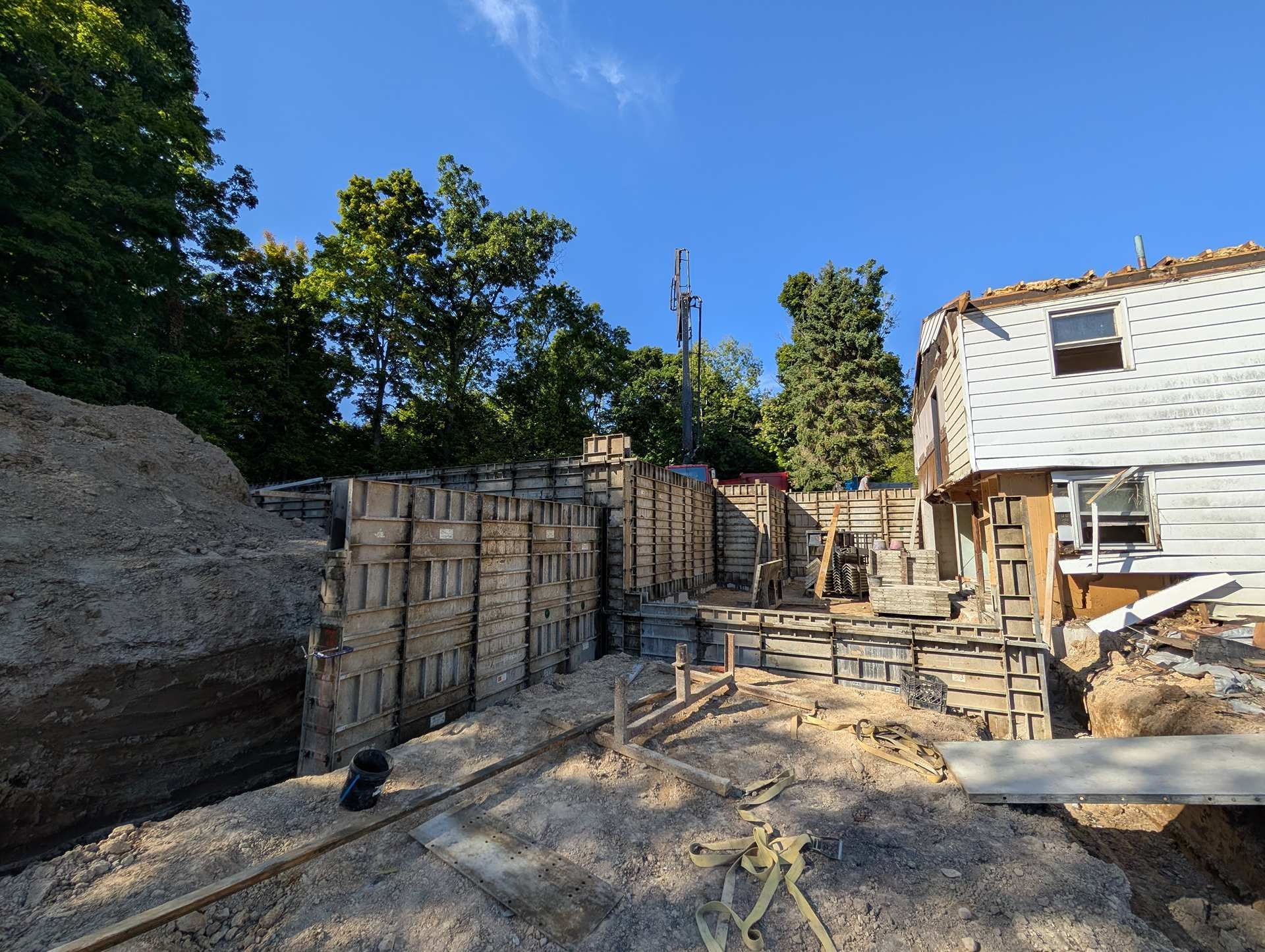 Foundation work in progress at a residential construction site with wooden concrete forms, dirt, and an adjacent house.