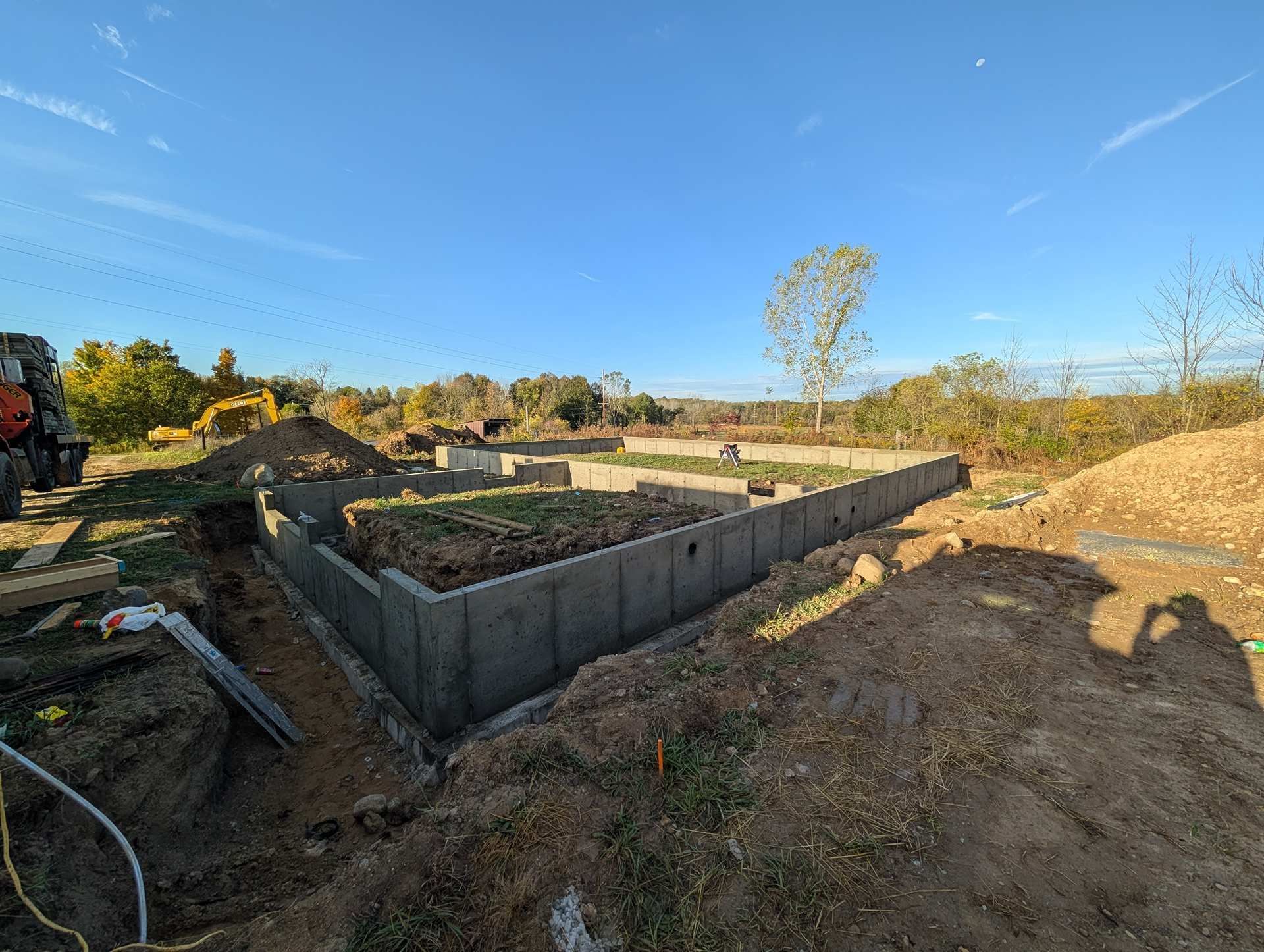 Concrete foundation walls for a new house under construction on a sunny, grassy lot with piles of dirt nearby.