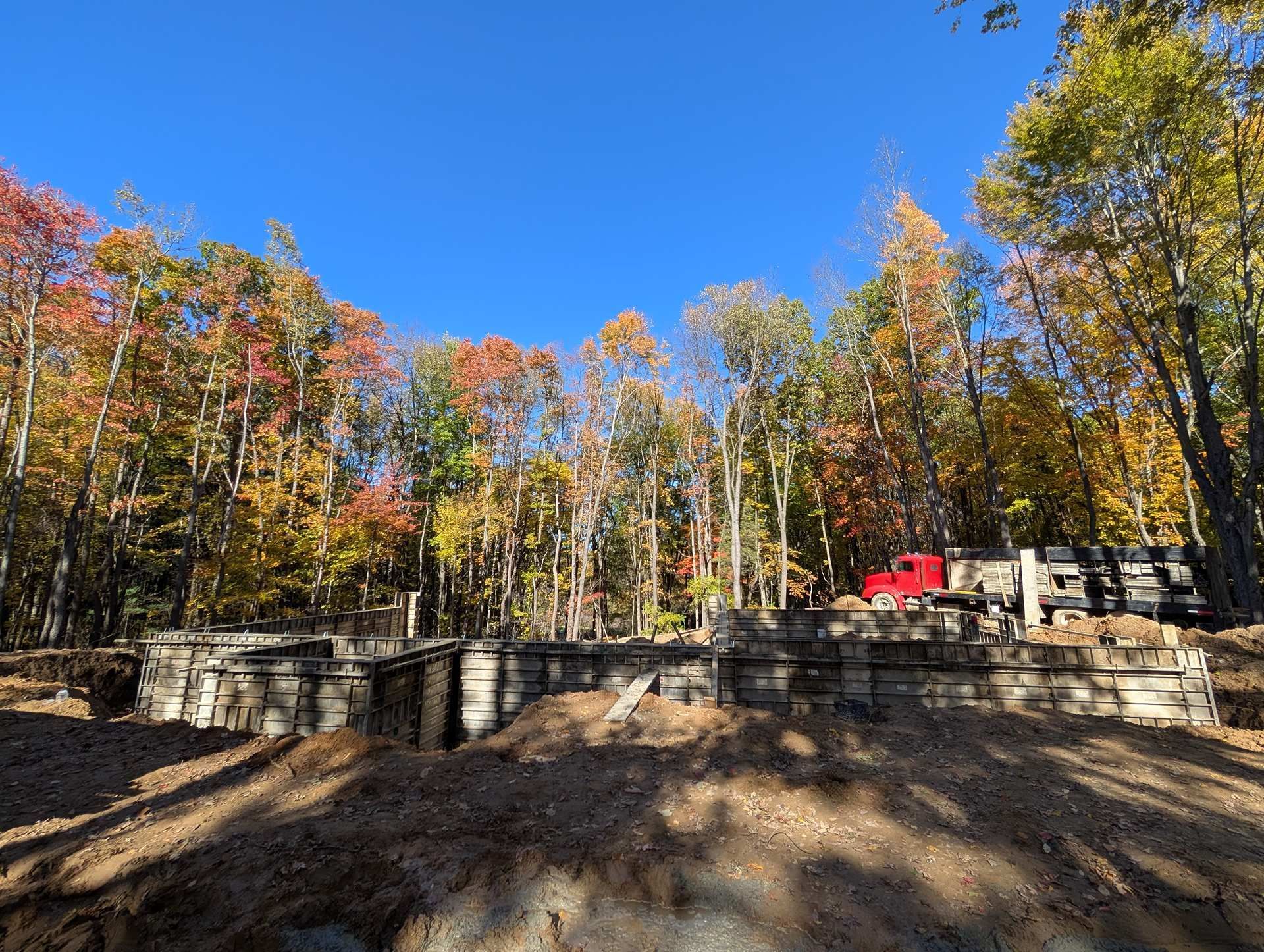 A concrete foundation under construction in a wooded area with autumn trees and a red truck in the background.