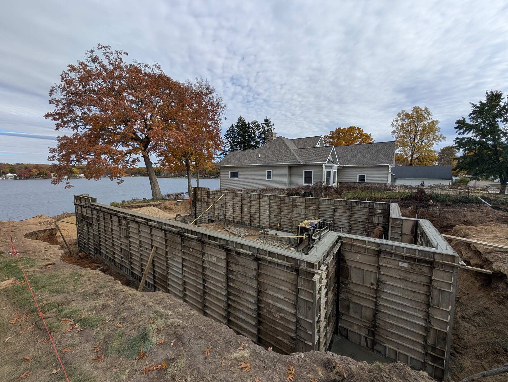 A view of a building foundation under construction with metal forms, located near a lake and trees on an autumn day.