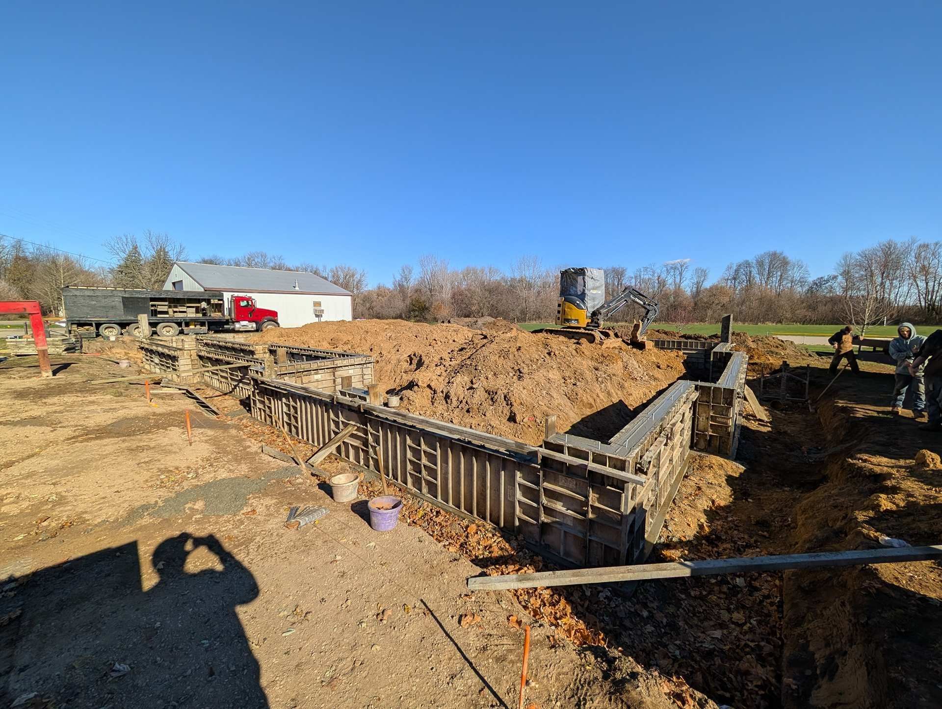 A construction site showing foundation walls being poured for a building in a rural area under a clear blue sky.